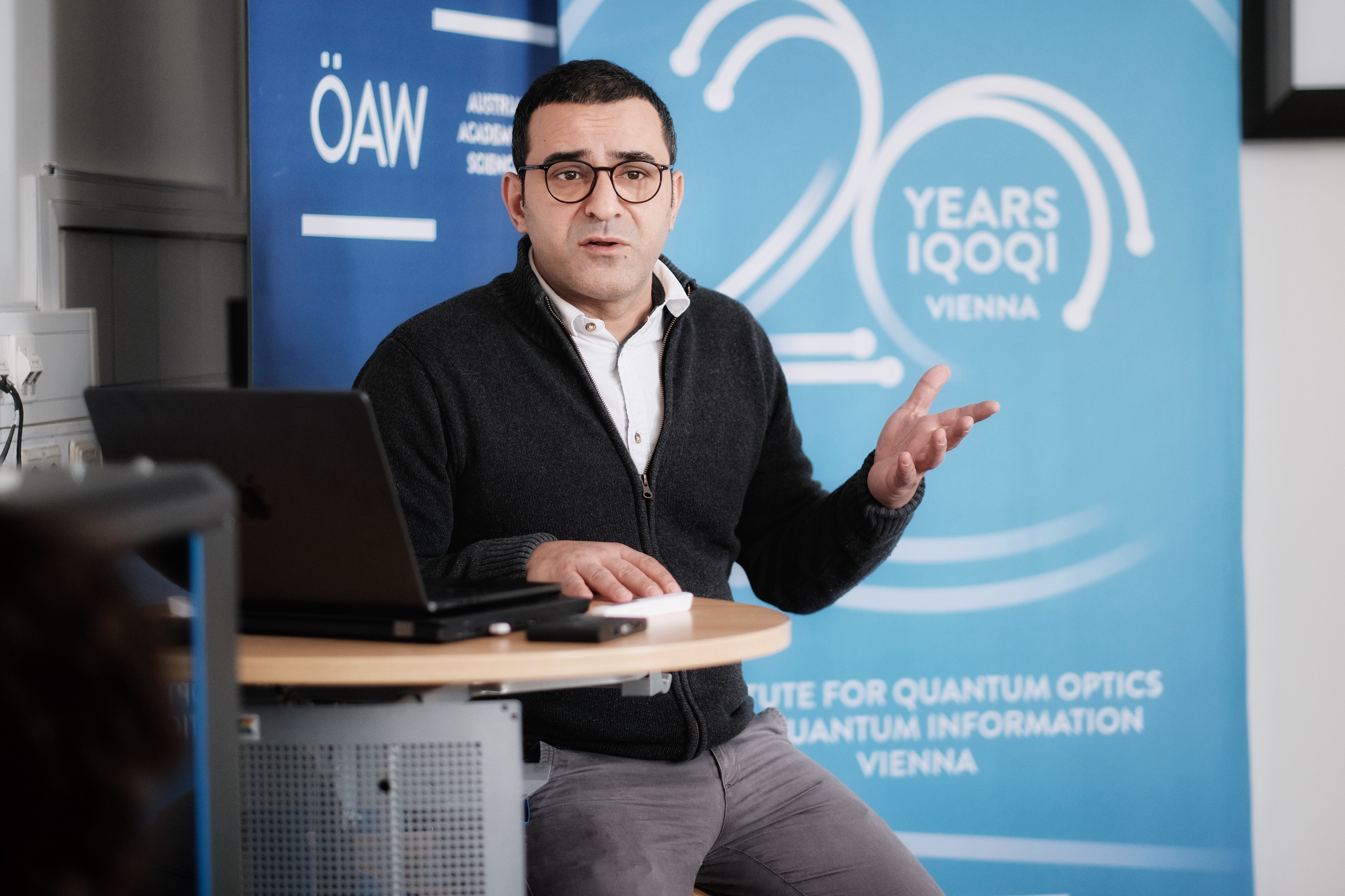 Scientist sitting in front of the IQOQI Vienna and Austrian Academy of Science' roll ups