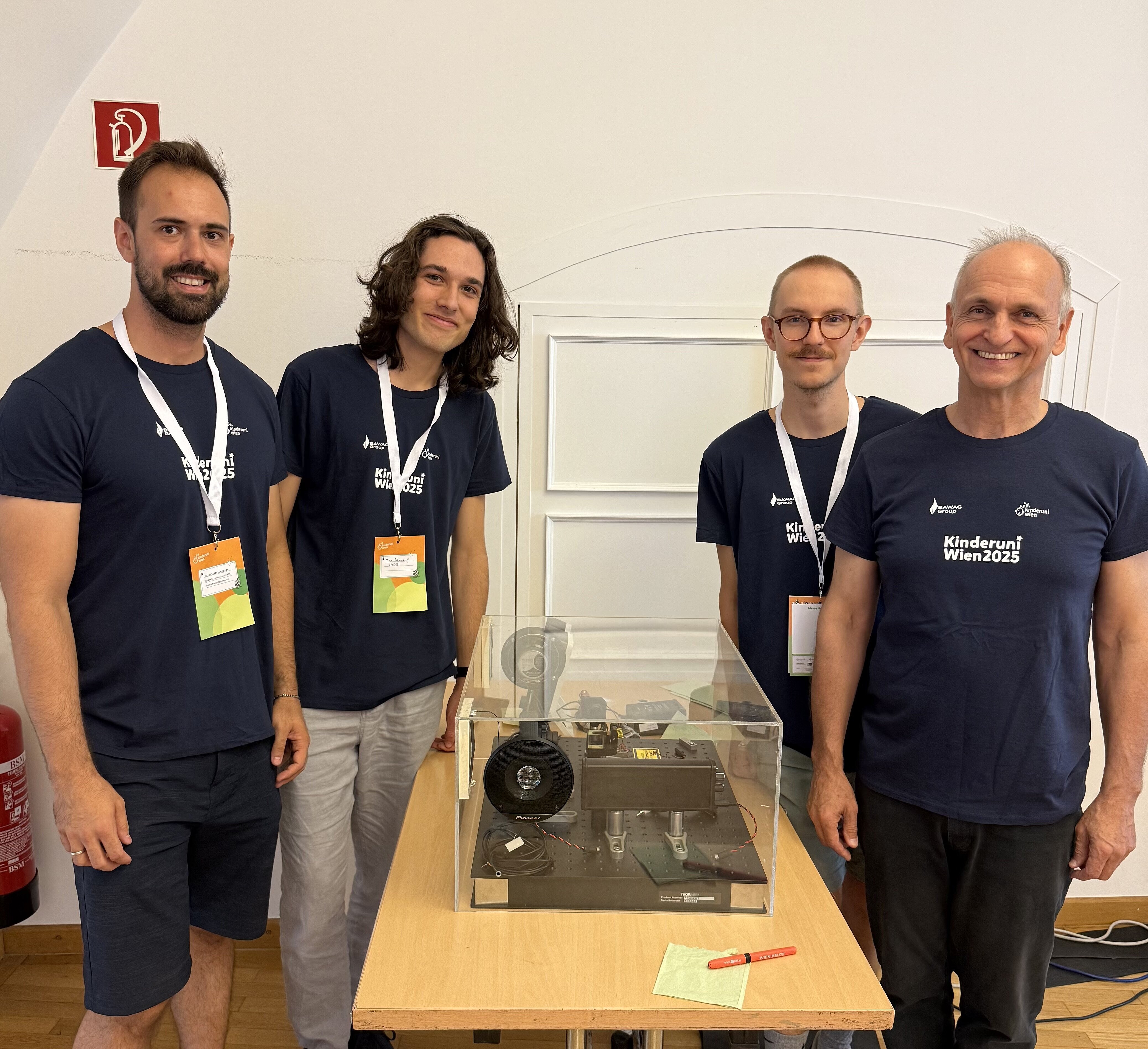 Four of our researchers wearing the official Children's University T-Shirts, and standing next to one of the experiments