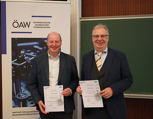 The two Ehrenfest winners holding their Award Certificates in front of the IQOQI Vienna roll up